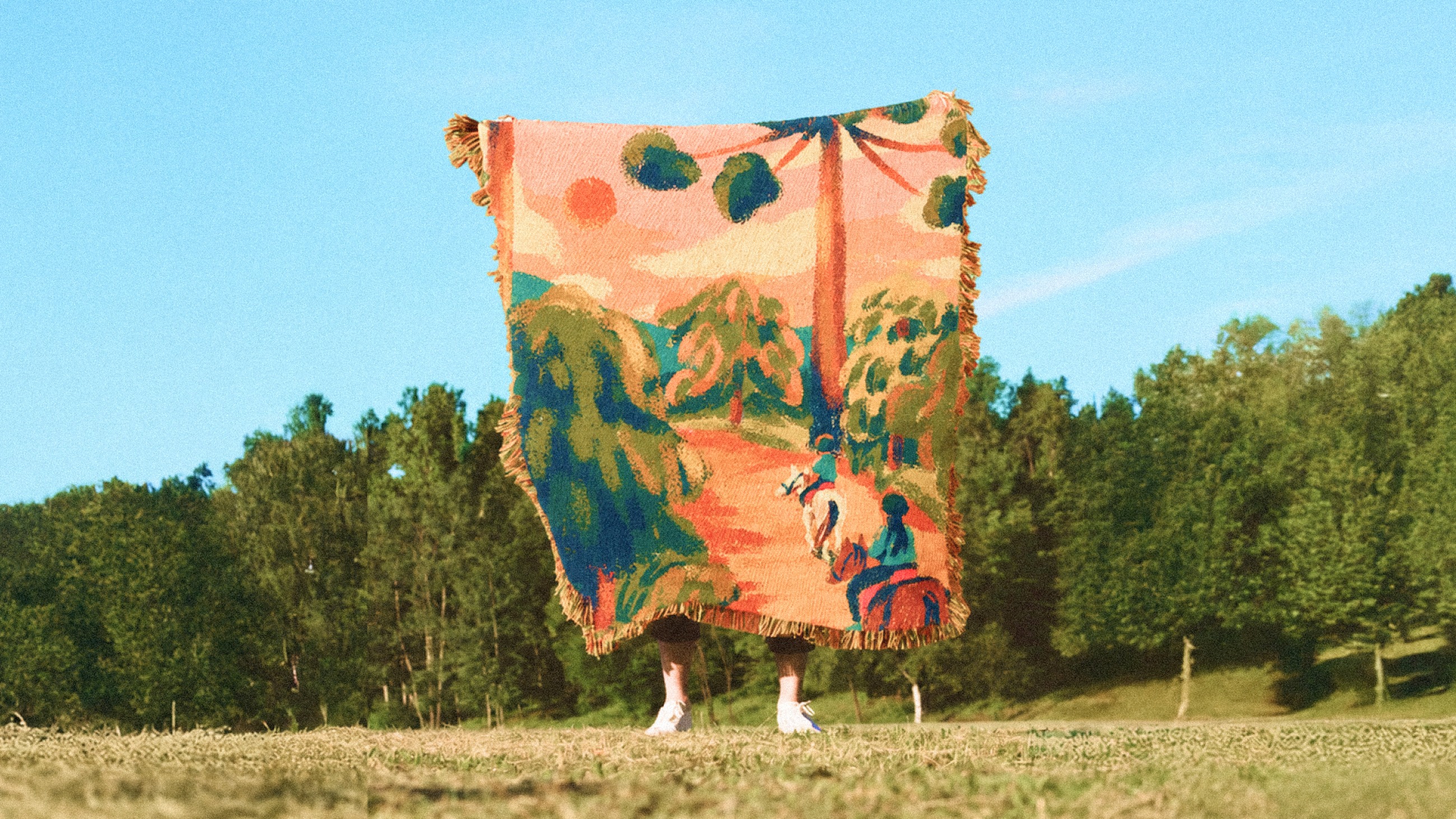 A woven blanket printed with an illustrated mountain scene, held open in a field